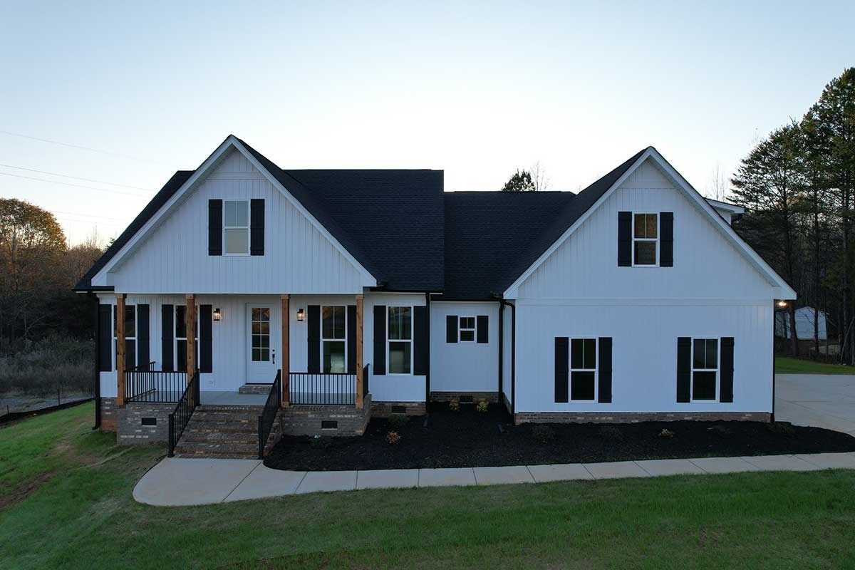 White two-story house with dark roof, front porch, and steps on a grassy lot at dusk