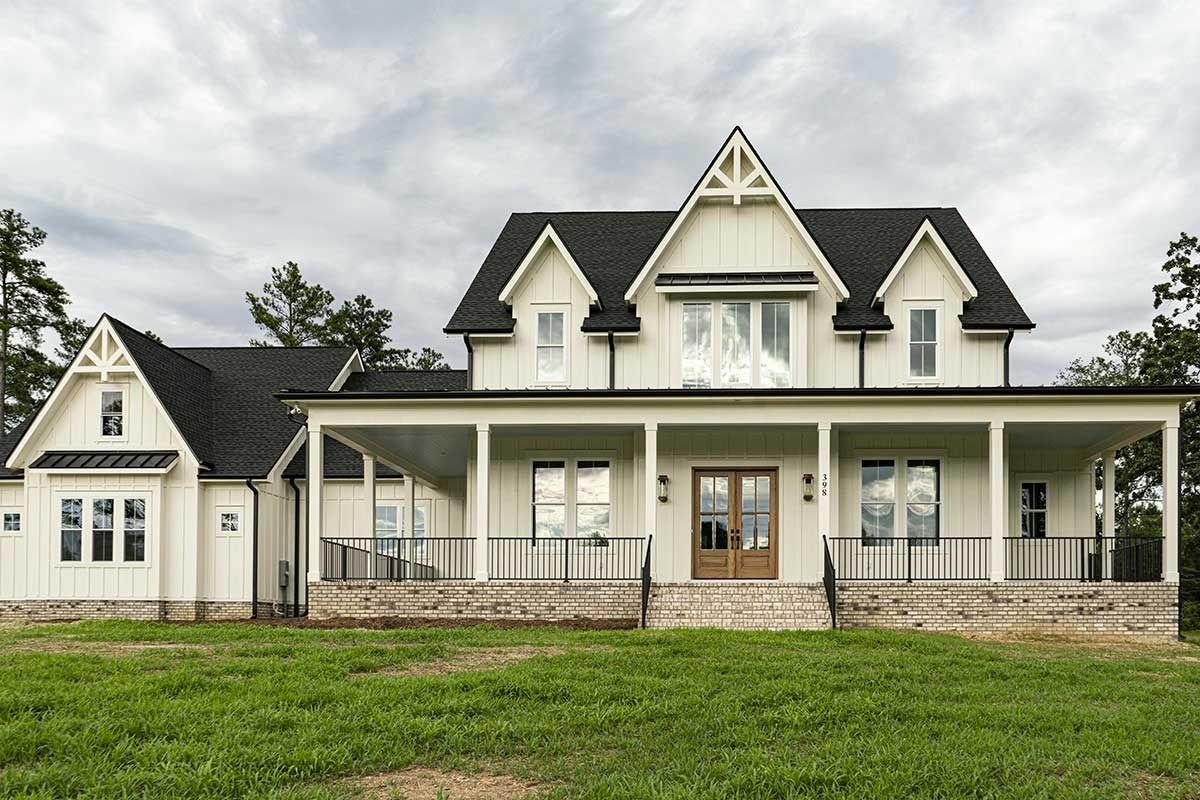 Large cream Victorian house with a wraparound porch and green lawn under an overcast sky