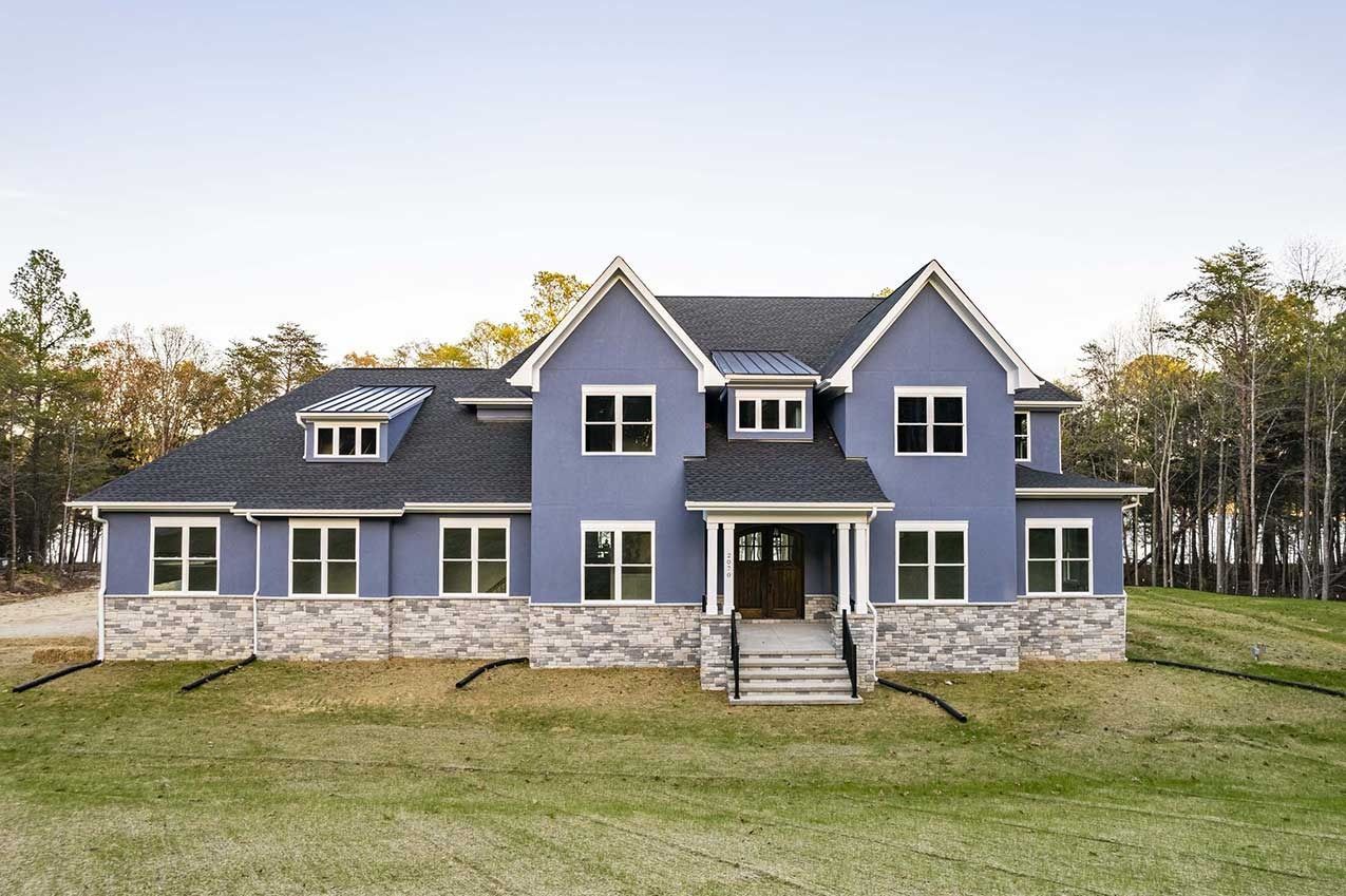 Blue two-story house with white trim and stone foundation on a grassy lawn.