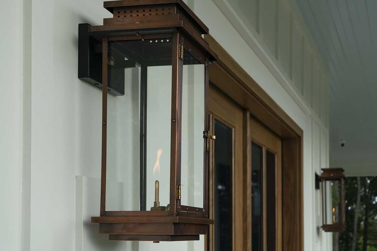 Wooden wall lantern with glass panels lit beside a house window and porch ceiling