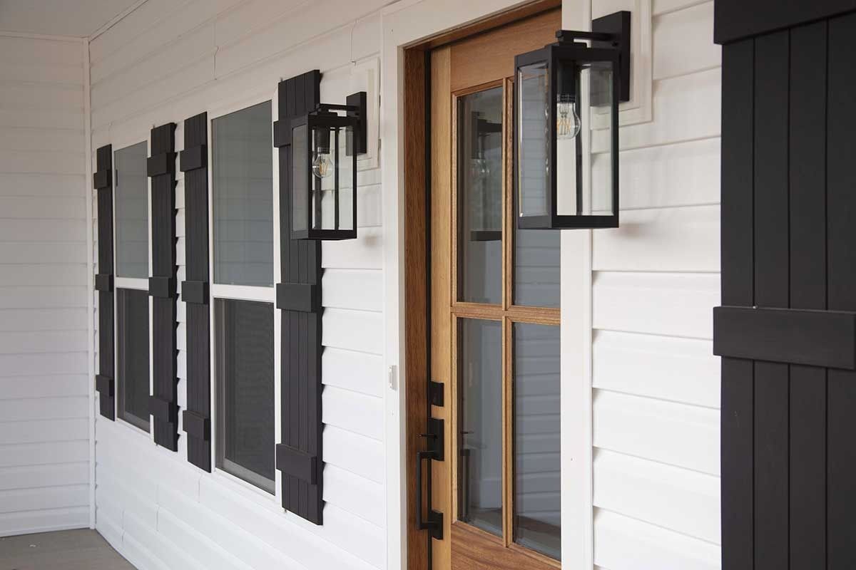 White house exterior with black shutters and lanterns beside a wooden glass door