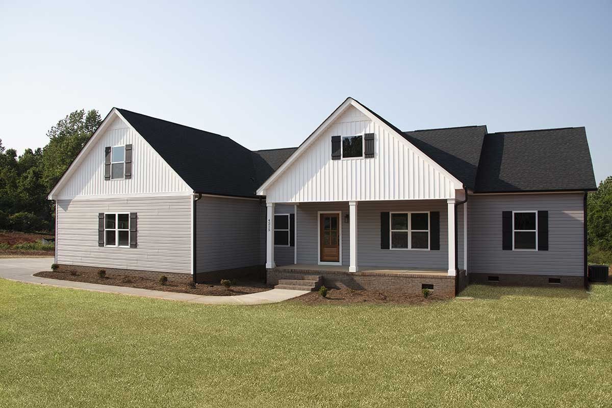 Gray farmhouse-style house with black roof and front porch on a grassy lot
