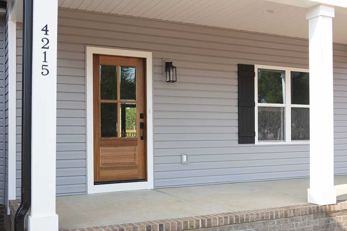 Front porch of a house with gray siding, a wooden door, white columns, and address number 4215.