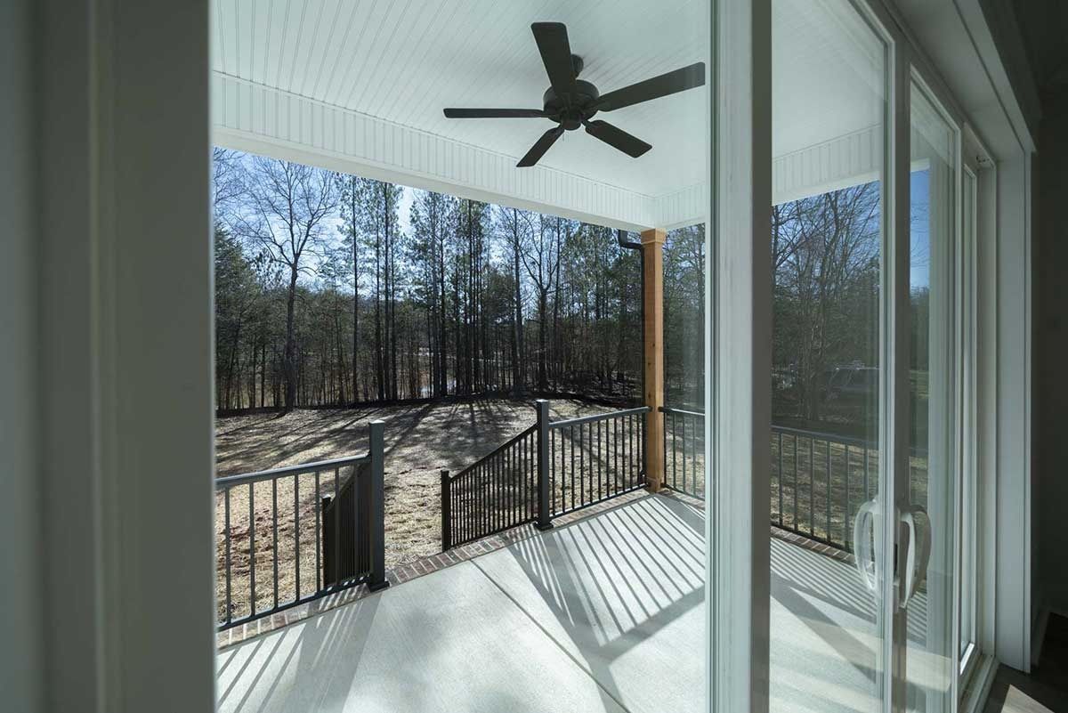Covered porch with black ceiling fan, railing, and a view of trees and yard beyond sliding glass doors