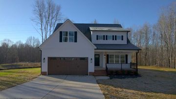 Two-story white house with attached garage, front porch, and large driveway on a sunny day