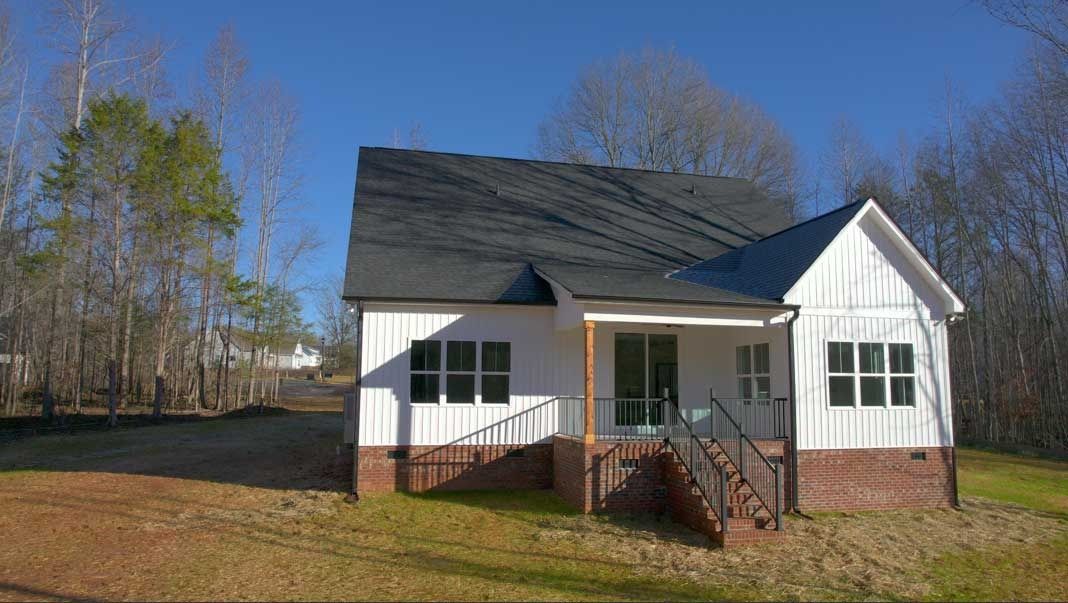 Small white house with black roof, front porch, and red-brown trim on a sunny day.