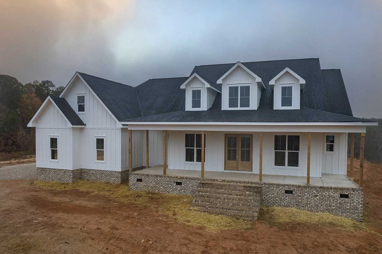 New white house with dark roof and stone porch on a bare lot under a cloudy sky