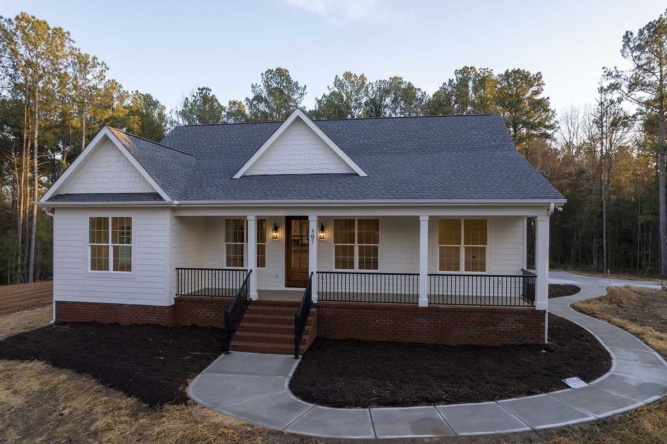 White single-story house with front porch, dark roof, and curved walkway at dusk