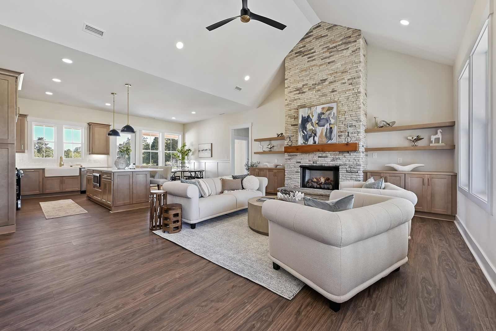 Bright open living room with white sofas, stone fireplace, and kitchen in the background