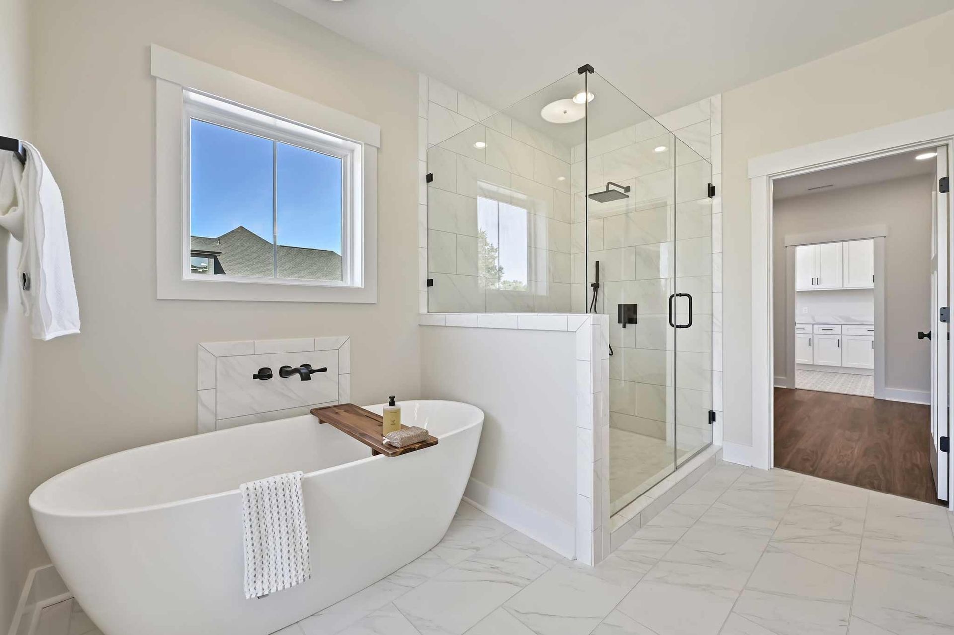Modern white bathroom with freestanding tub, glass shower, and vanity under a window