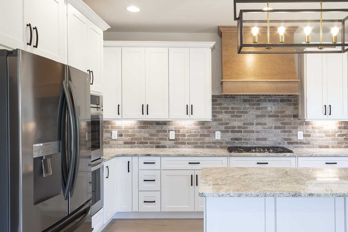 Modern kitchen with white cabinets, stainless steel fridge, granite island, and mosaic tile backsplash