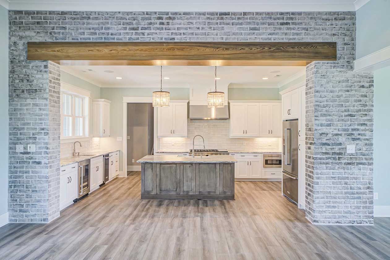 Bright modern kitchen with white cabinets, gray brick walls, and a large wood island
