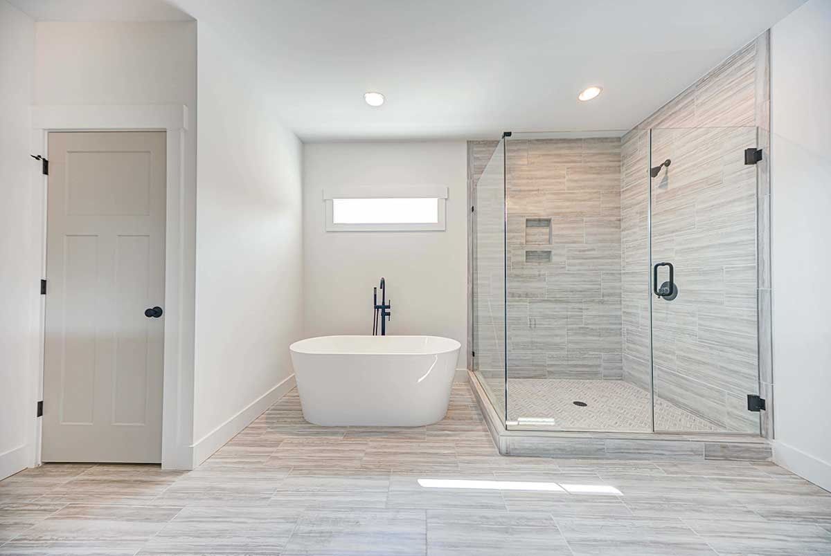 Modern white bathroom with freestanding tub, walk-in glass shower, and gray tile floor