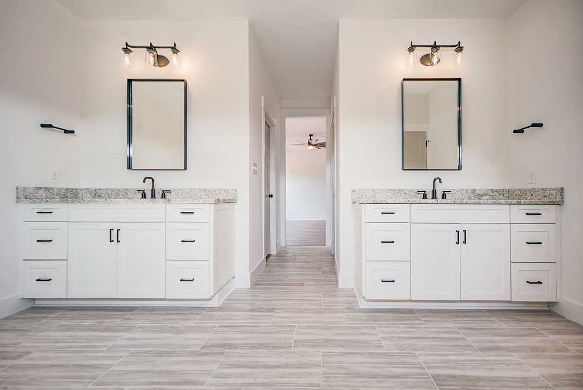 Bright double vanity bathroom with mirrors, sconces, white cabinets, and wood-look tile floor.