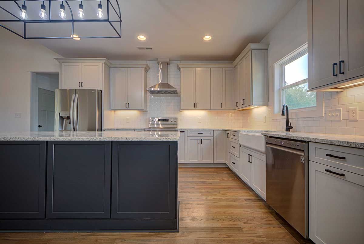Modern kitchen with dark island, white cabinets, stainless appliances, and wood floors