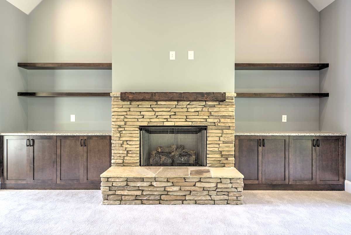 Living room with stone fireplace, built-in shelves, and dark wood cabinets on both sides.
