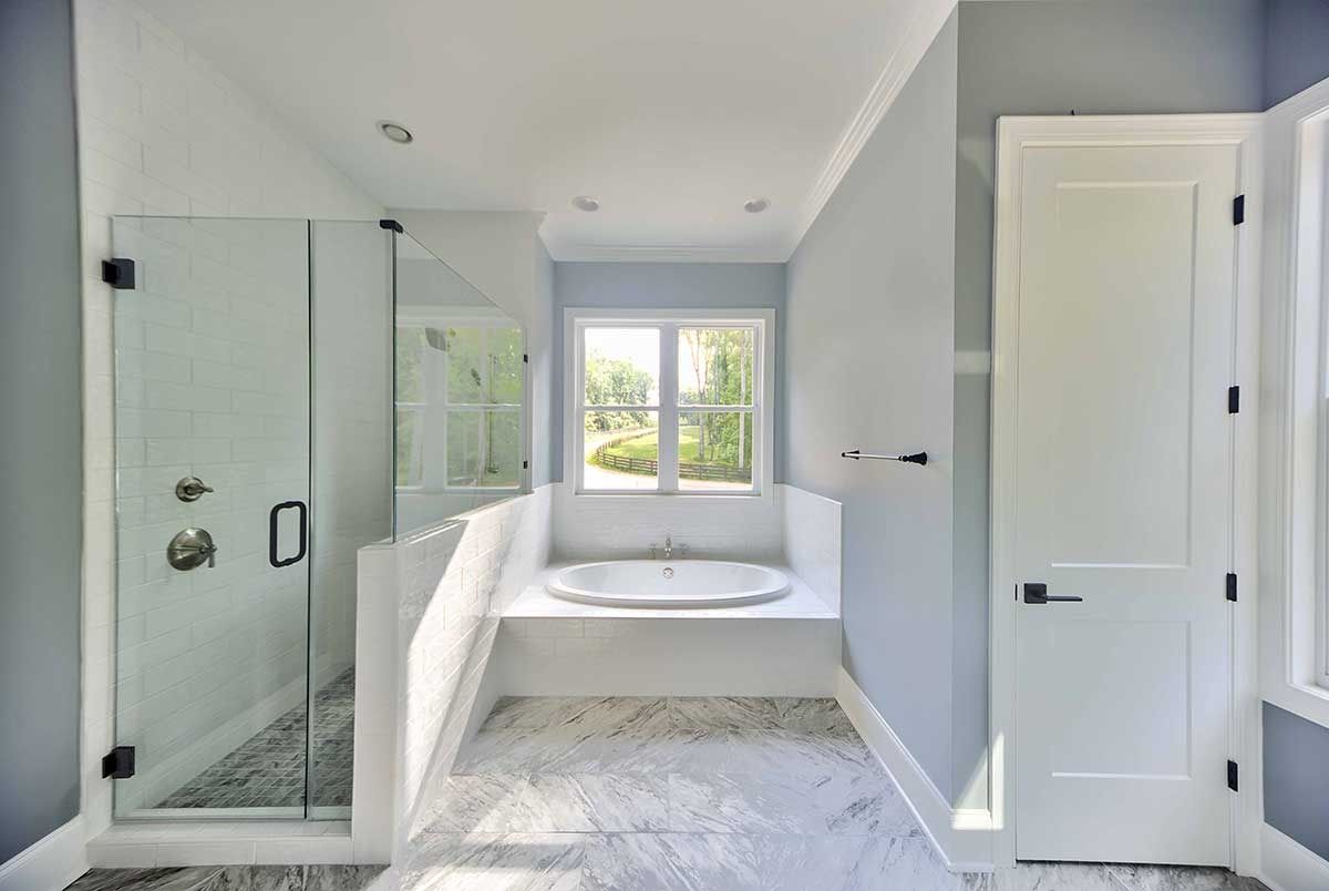 Bright modern bathroom with a glass shower, double vanity, and windowed mirror light.