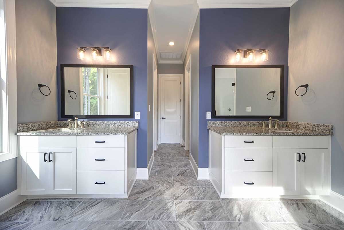 Bright double bathroom vanity with white cabinets, gray countertops, mirrors, and patterned tile floor.