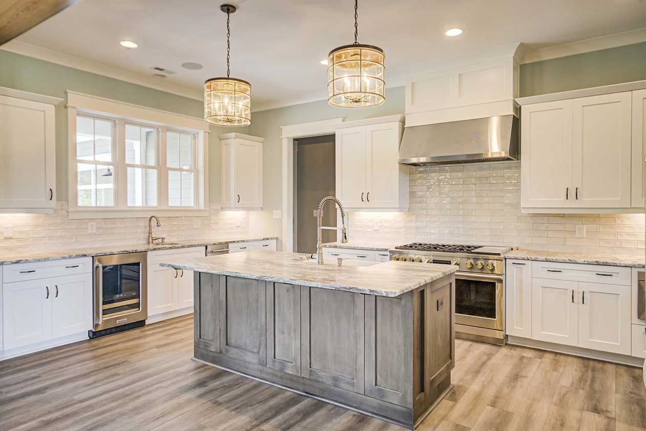 Bright modern kitchen with white cabinets, marble island, pendant lights, and stainless steel appliances