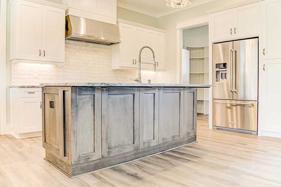Bright modern kitchen with white cabinets, gray island, and stainless steel refrigerator