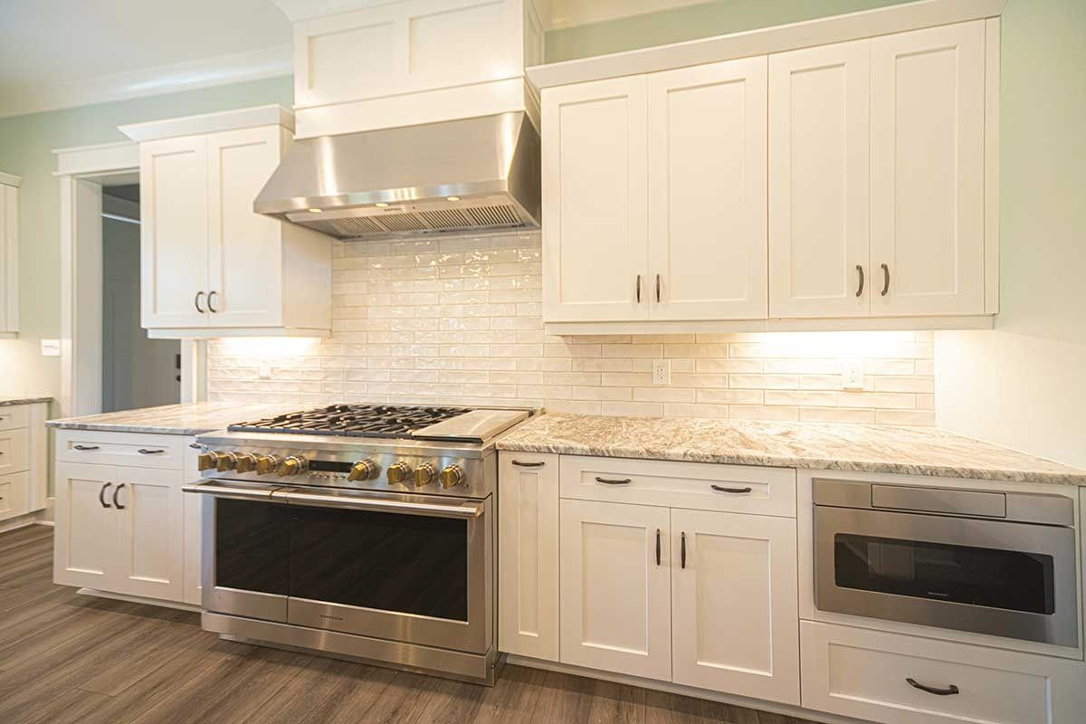 Bright white kitchen with marble counters, stainless steel stove and hood, and built-in microwave oven