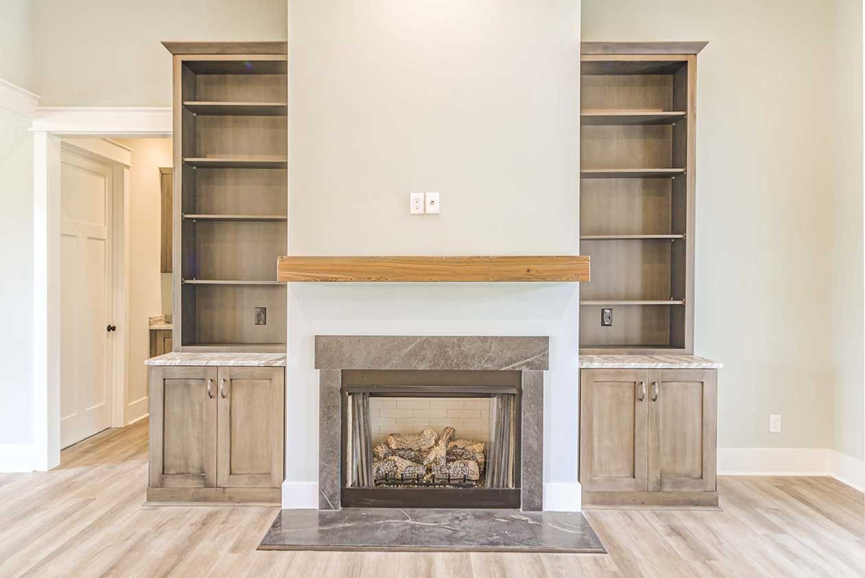 Empty living room with built-in shelves flanking a gray fireplace and light wood flooring