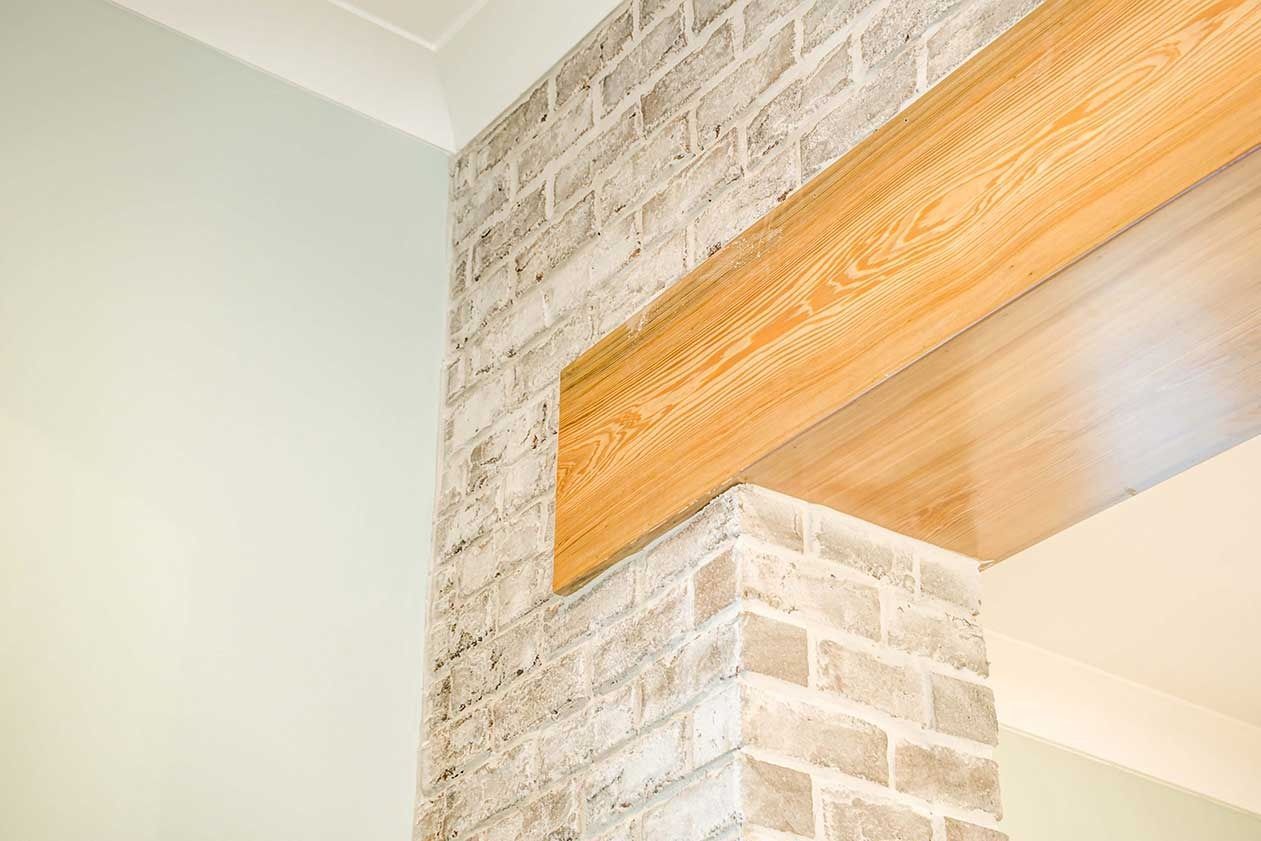 Close-up of a wood beam on a white brick wall near a pale green corner ceiling
