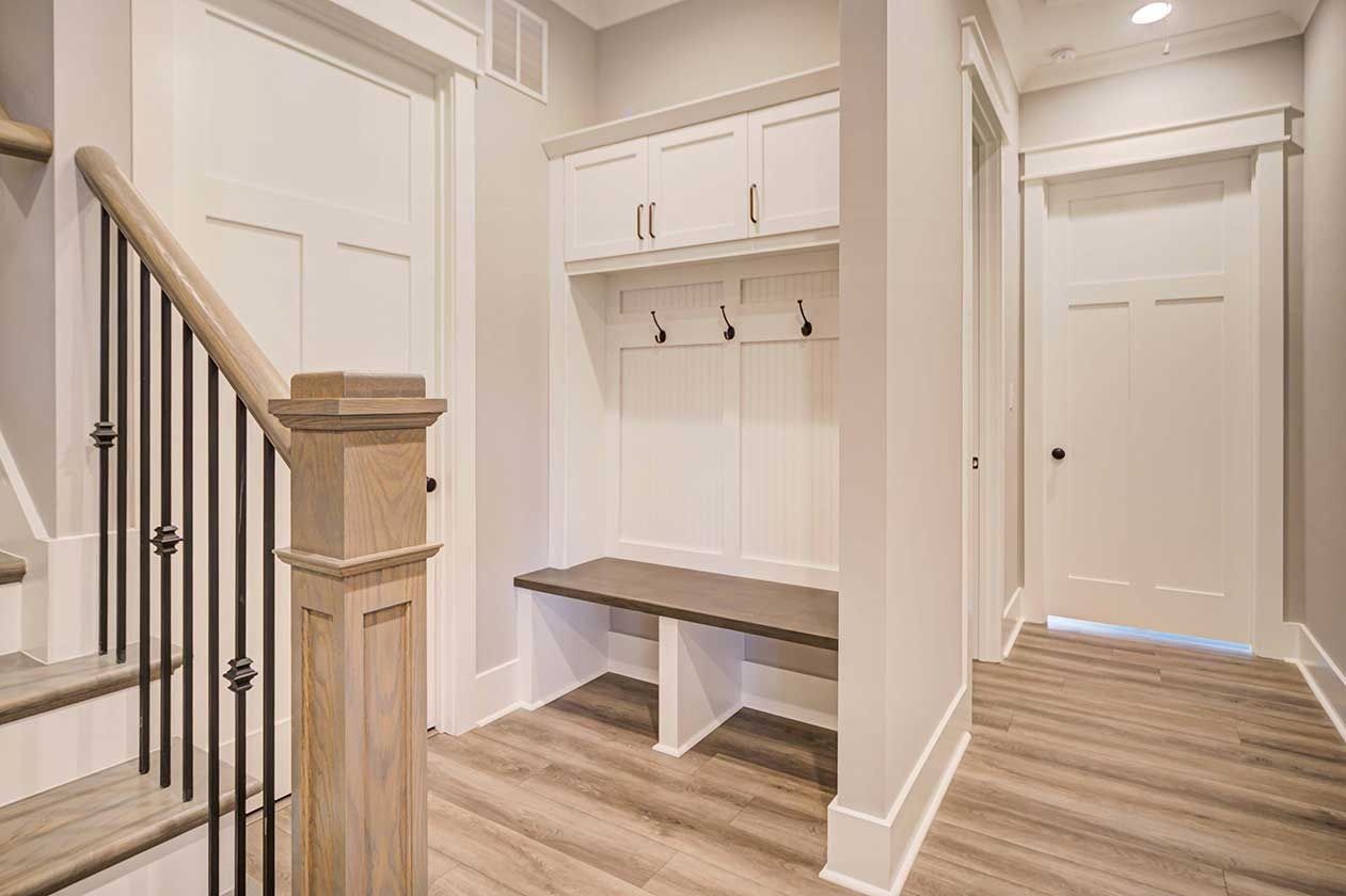 Bright entryway with staircase, built-in bench, coat hooks, and white doors on wood floors