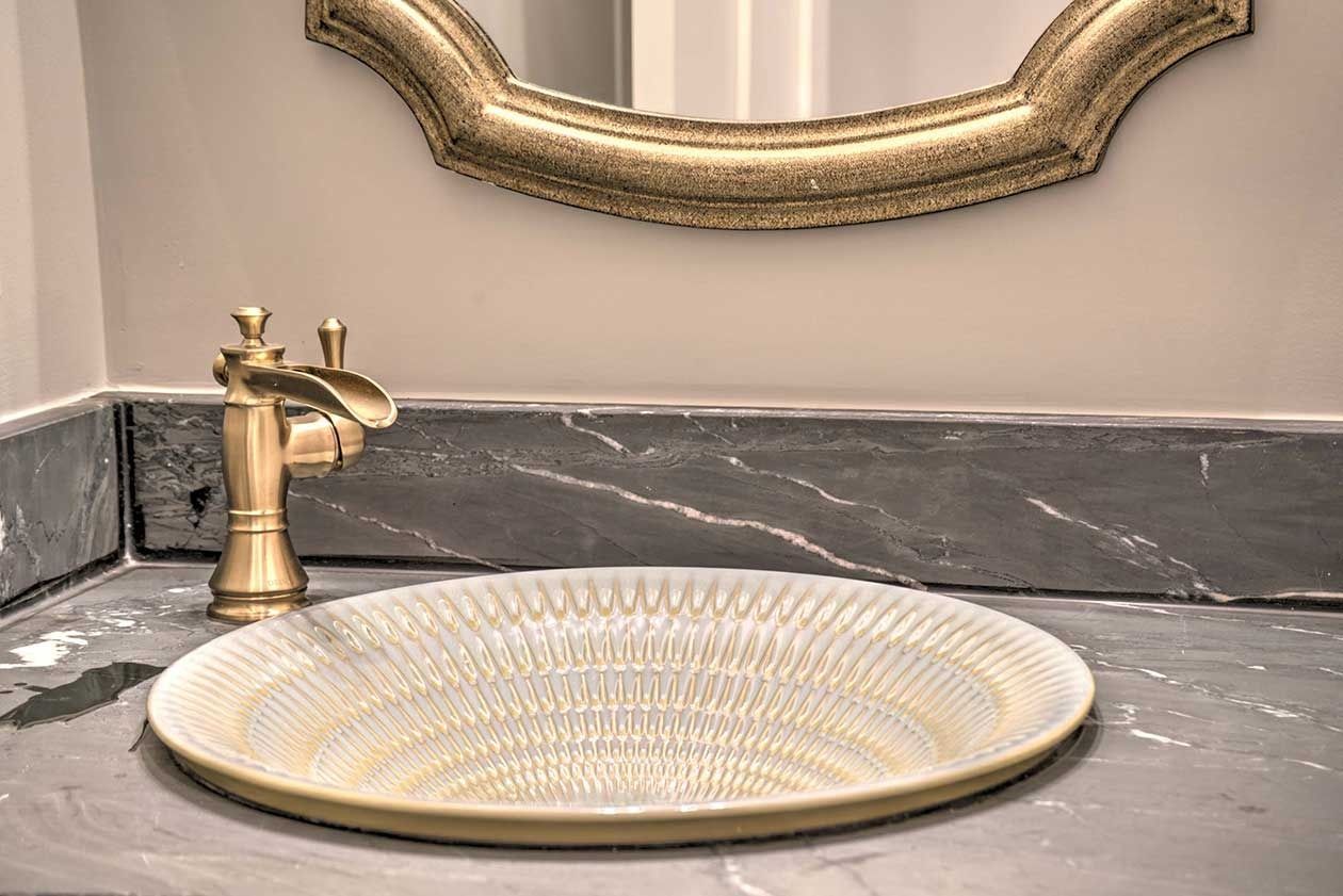 Gold faucet and decorative sink on a gray marble bathroom vanity under a framed mirror