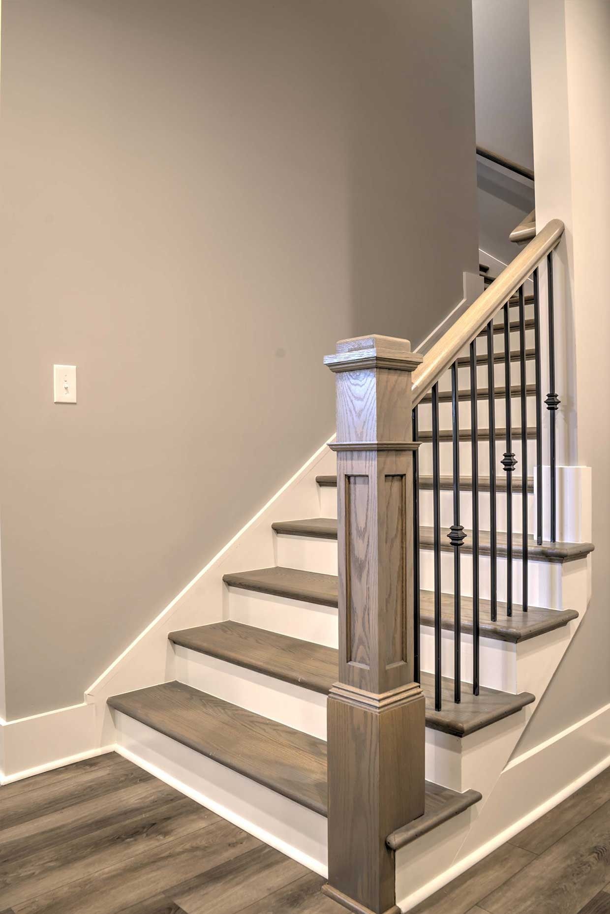 Indoor staircase with white steps, dark railing, and beige walls, viewed from the bottom.