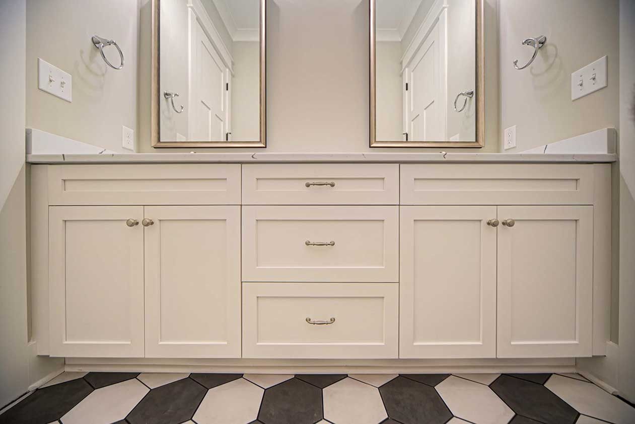 Double vanity bathroom with white cabinets, mirrors, and black-and-white patterned floor tiles
