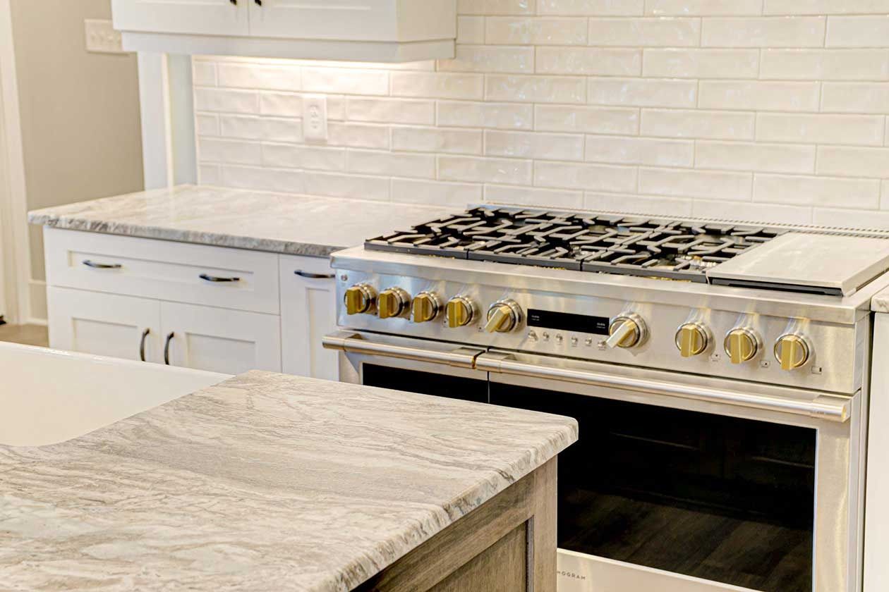 Modern kitchen with white cabinets, marble island, and stainless steel gas range