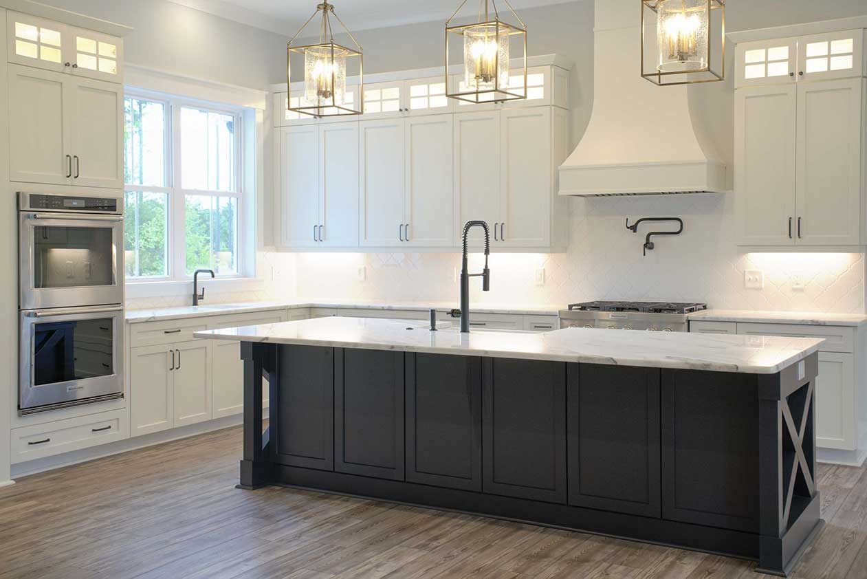 Modern white kitchen with black island, pendant lights, and large windows