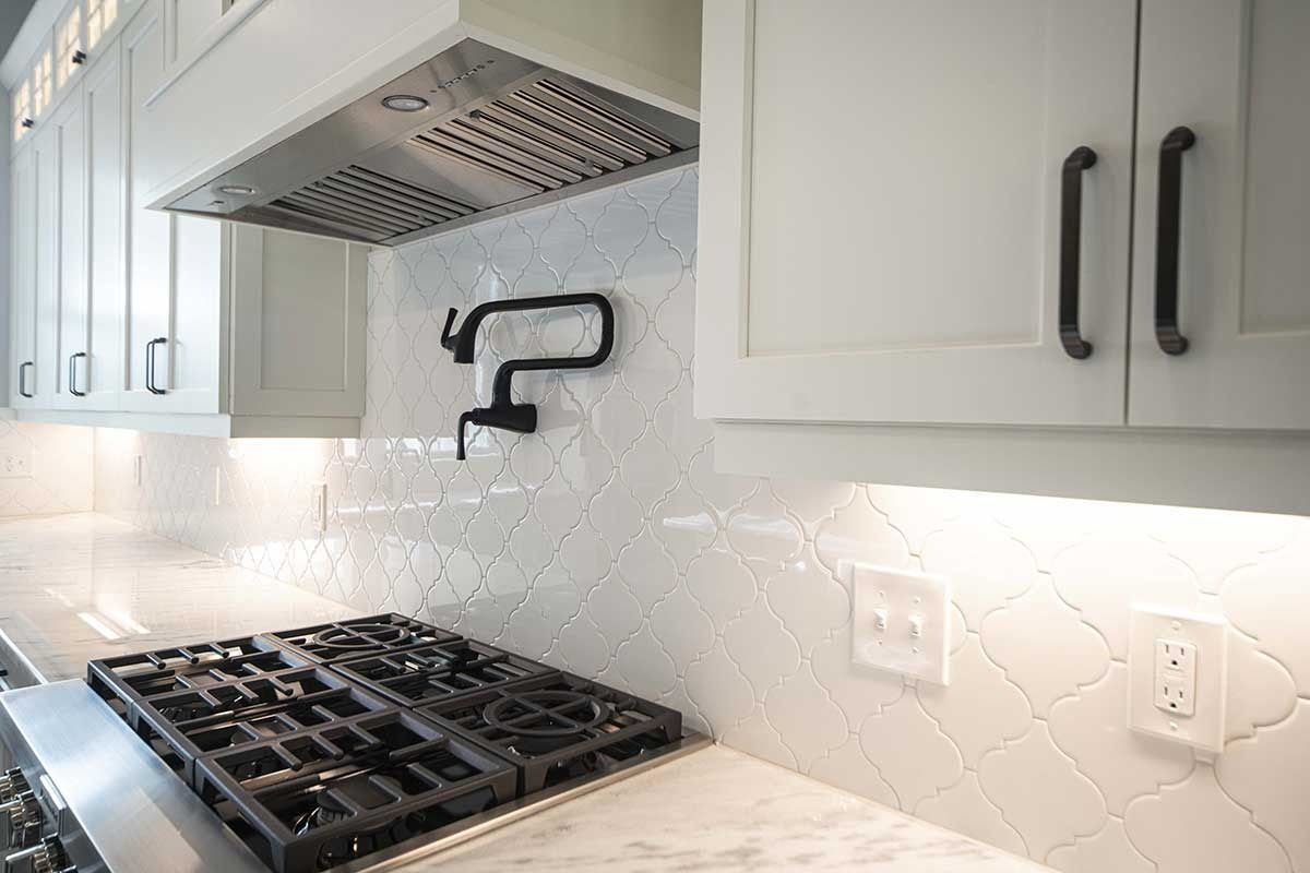 Modern kitchen with white cabinets, gas stove, black faucet, and herringbone tile backsplash