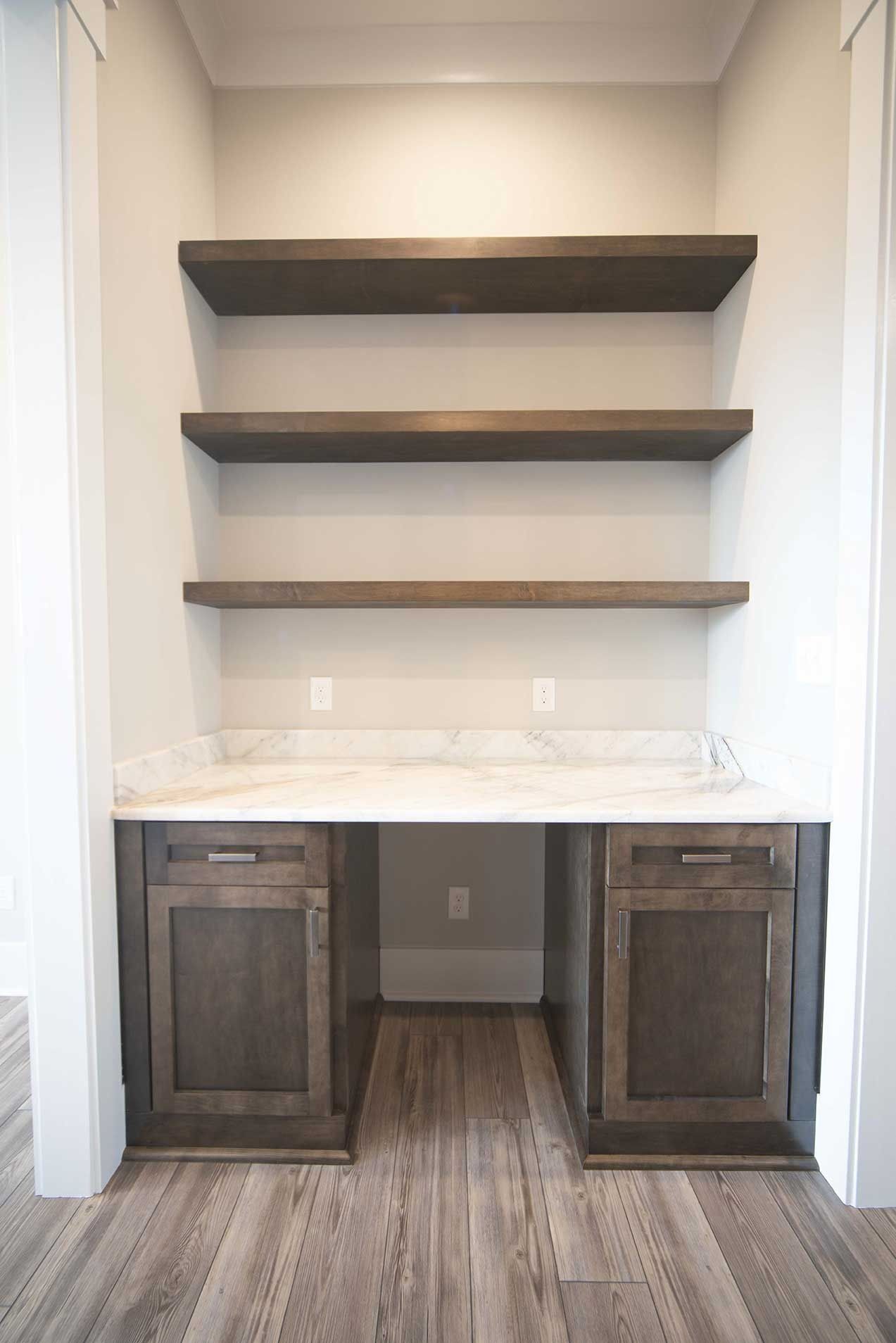 Built-in office nook with dark wood desk, white marble top, and three floating shelves.