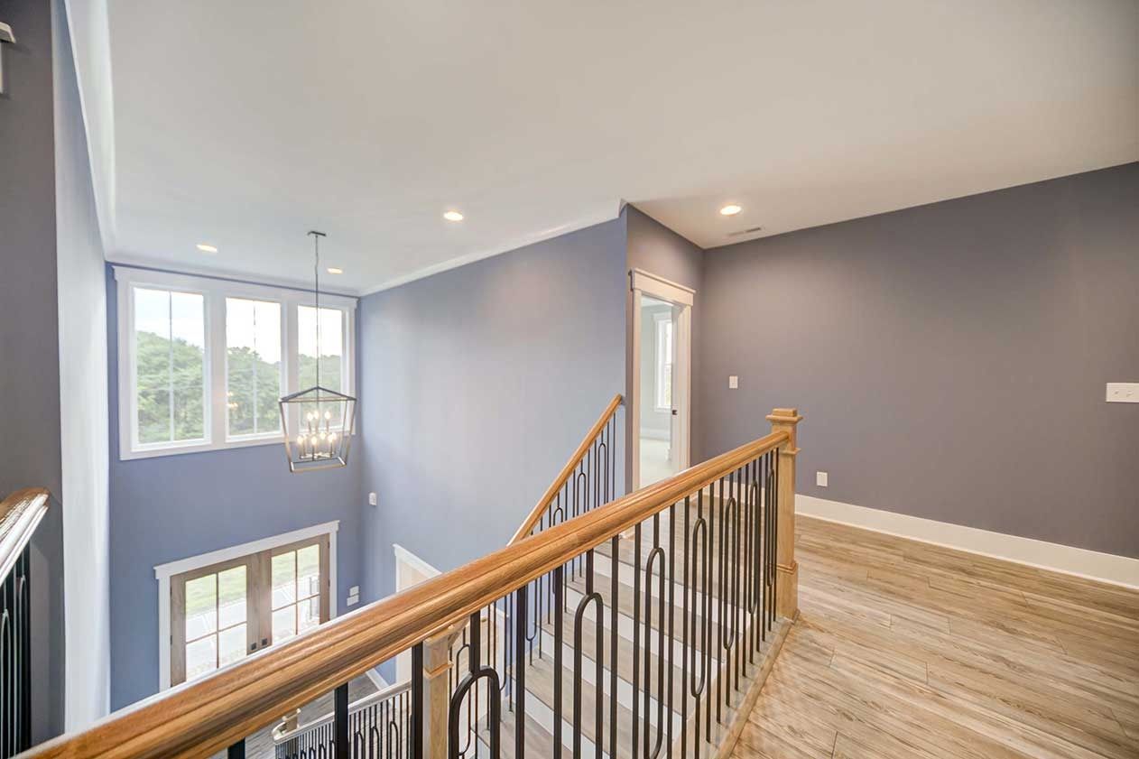 Stair landing with wood railing, gray walls, and large windows overlooking the lower floor
