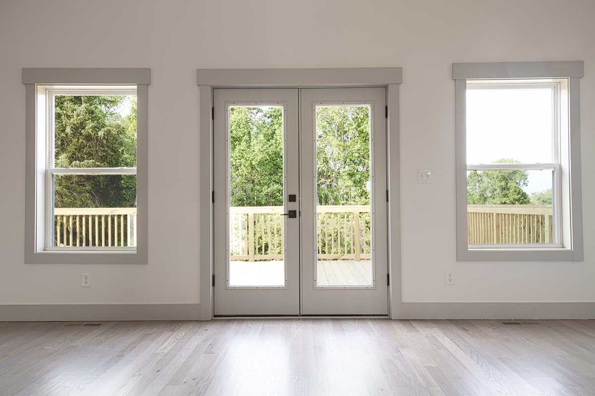 Bright empty room with white walls, hardwood floor, and three windows with a double glass door in the center.