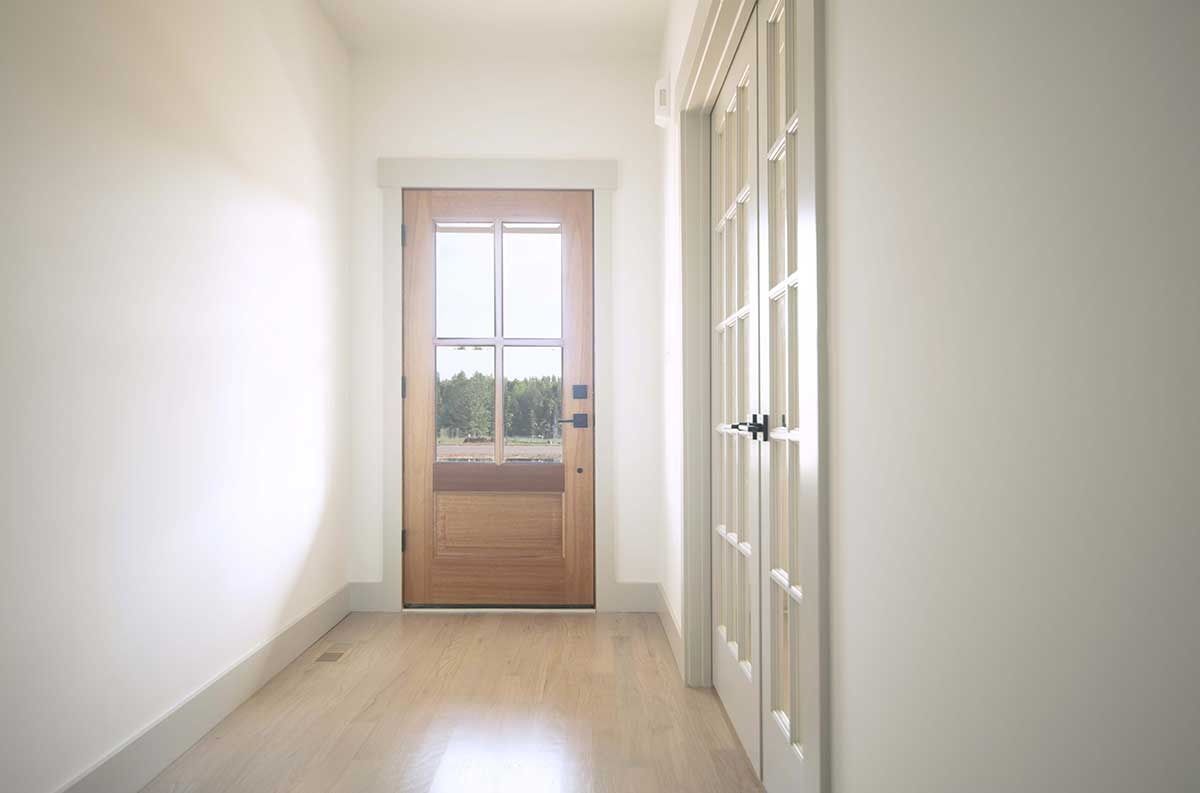 Bright empty hallway with white walls, wood floor, and a glass-paneled door at the end.