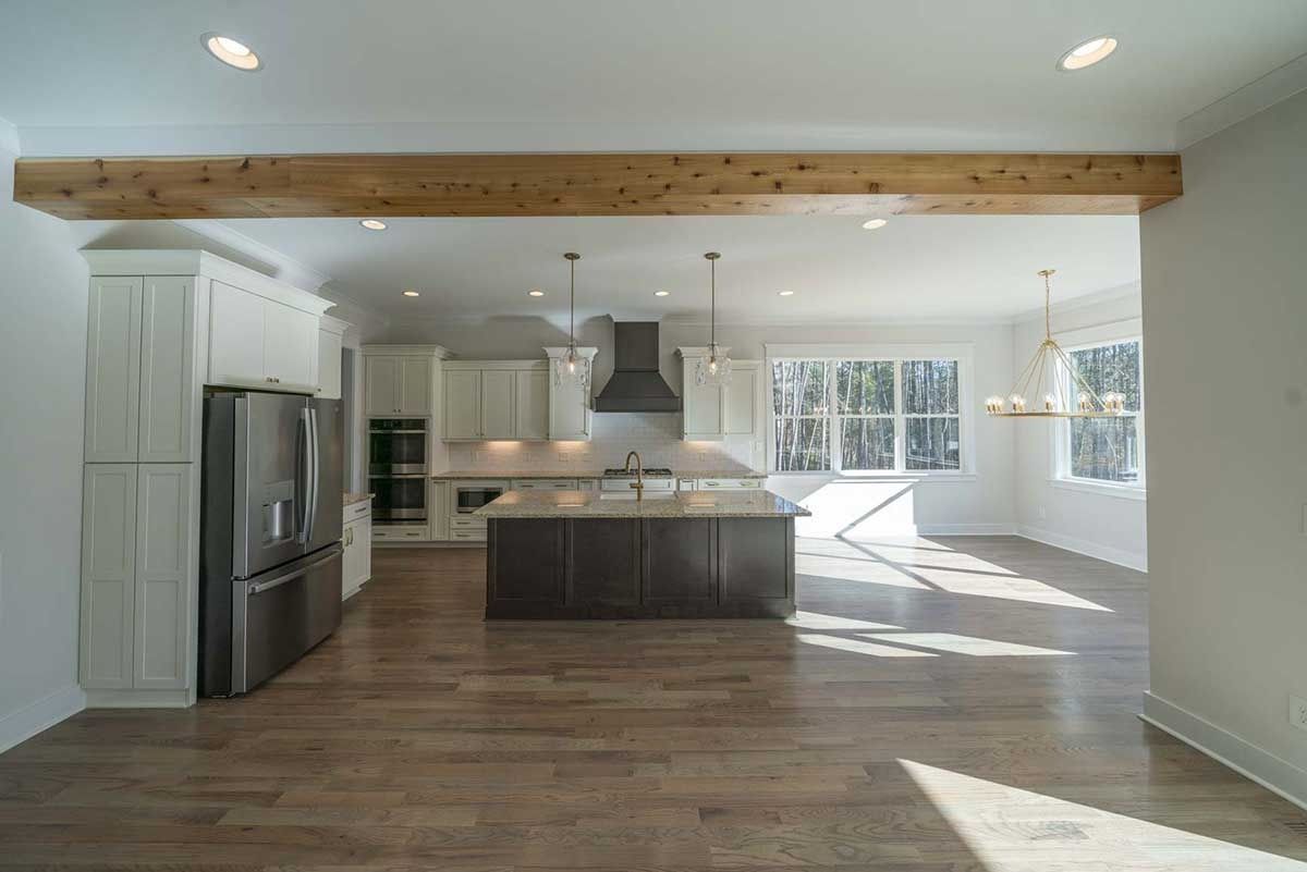 Spacious open-plan kitchen and living room with wood floors, exposed beam, and bright windows.