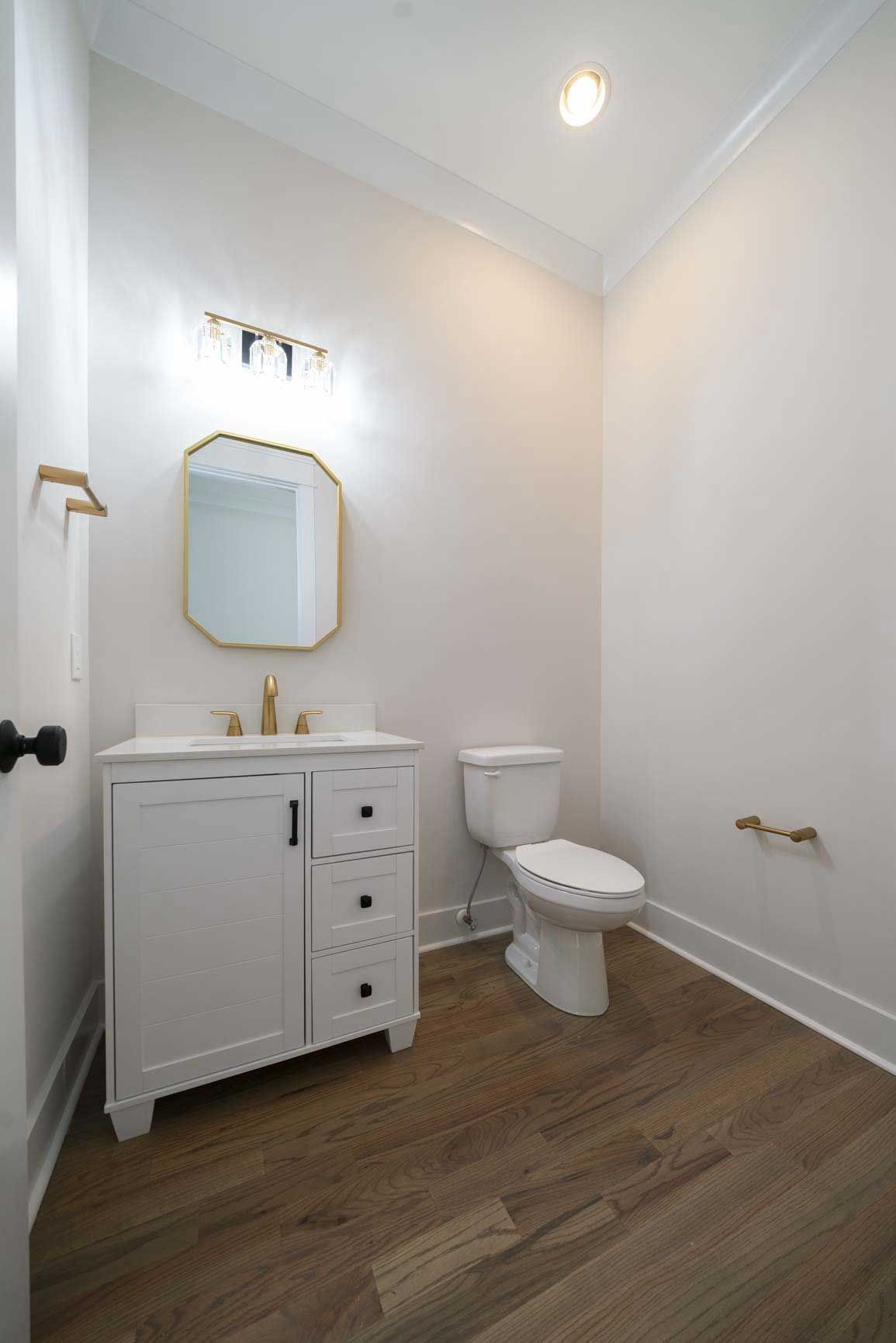Small white bathroom with vanity, mirror, toilet, and wood floor
