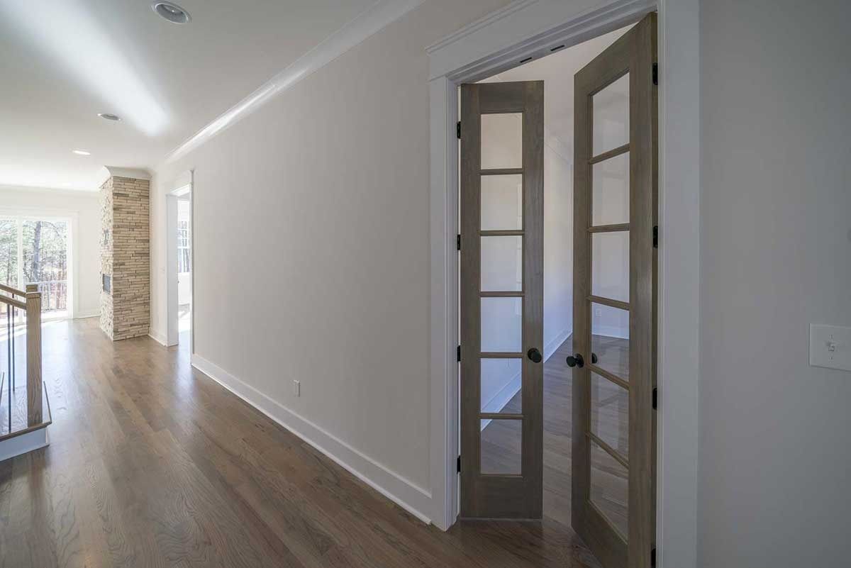 Bright hallway with hardwood floors and glass-paneled double doors leading into a sunlit room