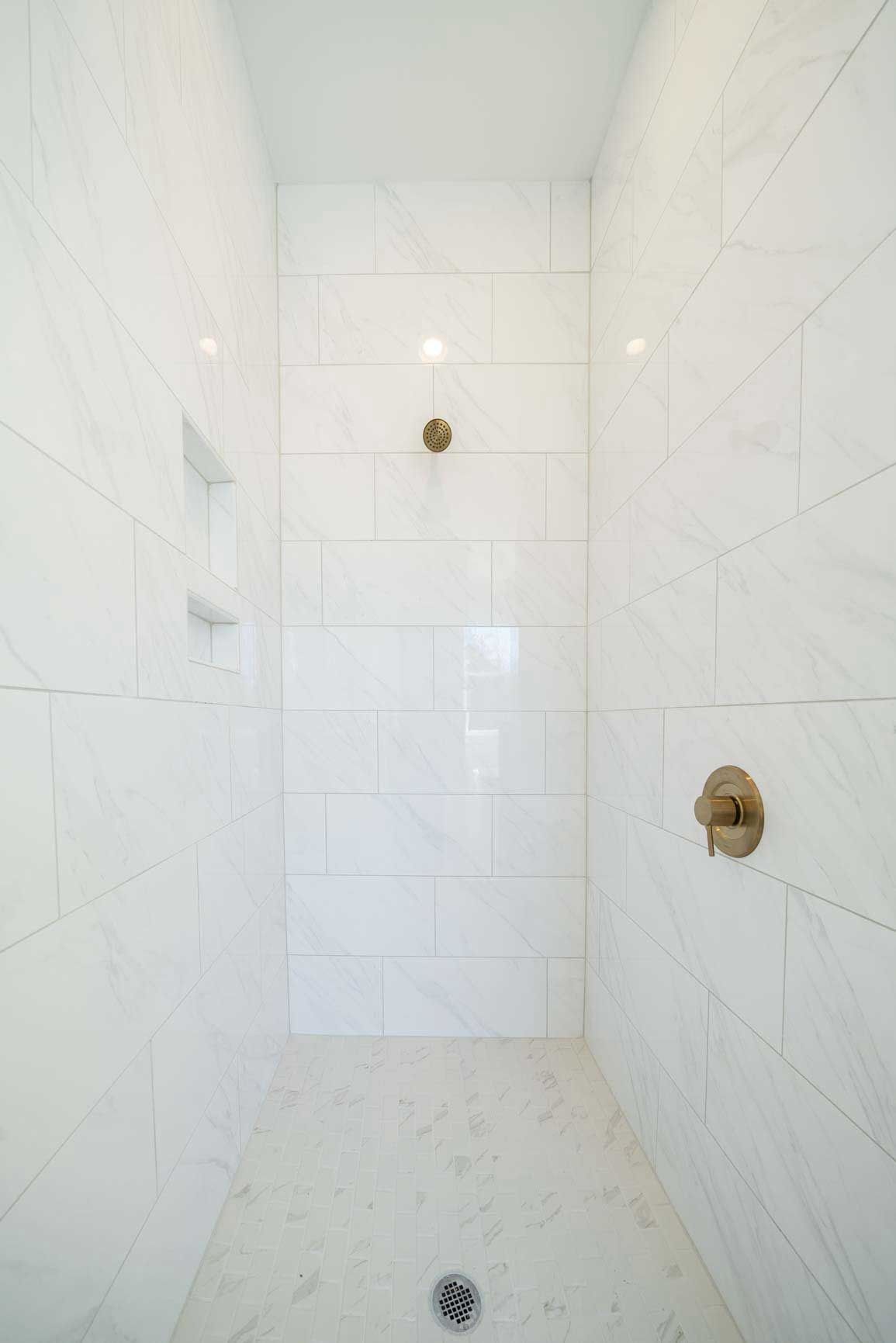 Empty white-tiled shower stall with three plumbing fixtures and a floor drain