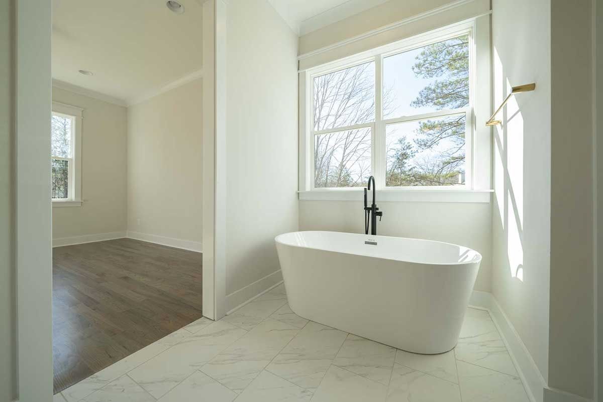 Bright minimalist bathroom with a freestanding tub, black faucet, and large window by an adjacent room.