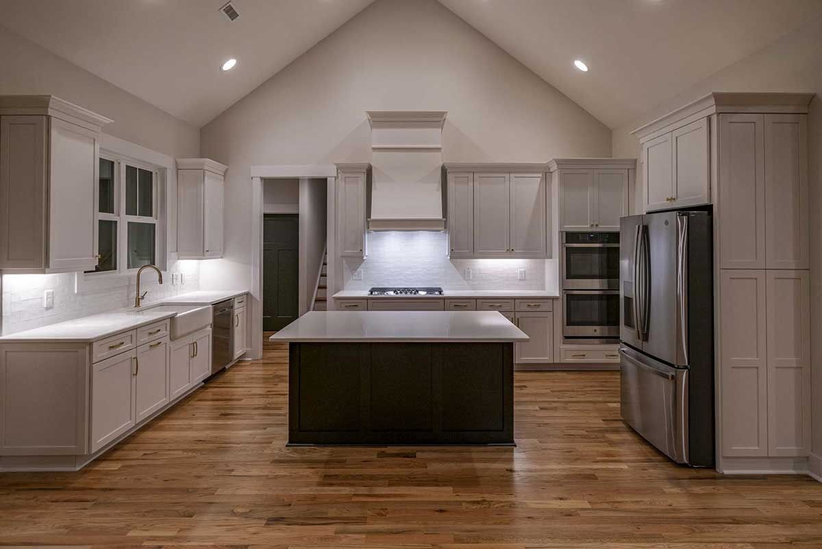 Spacious modern kitchen with white cabinets, black island, stainless steel appliances, and wood floors