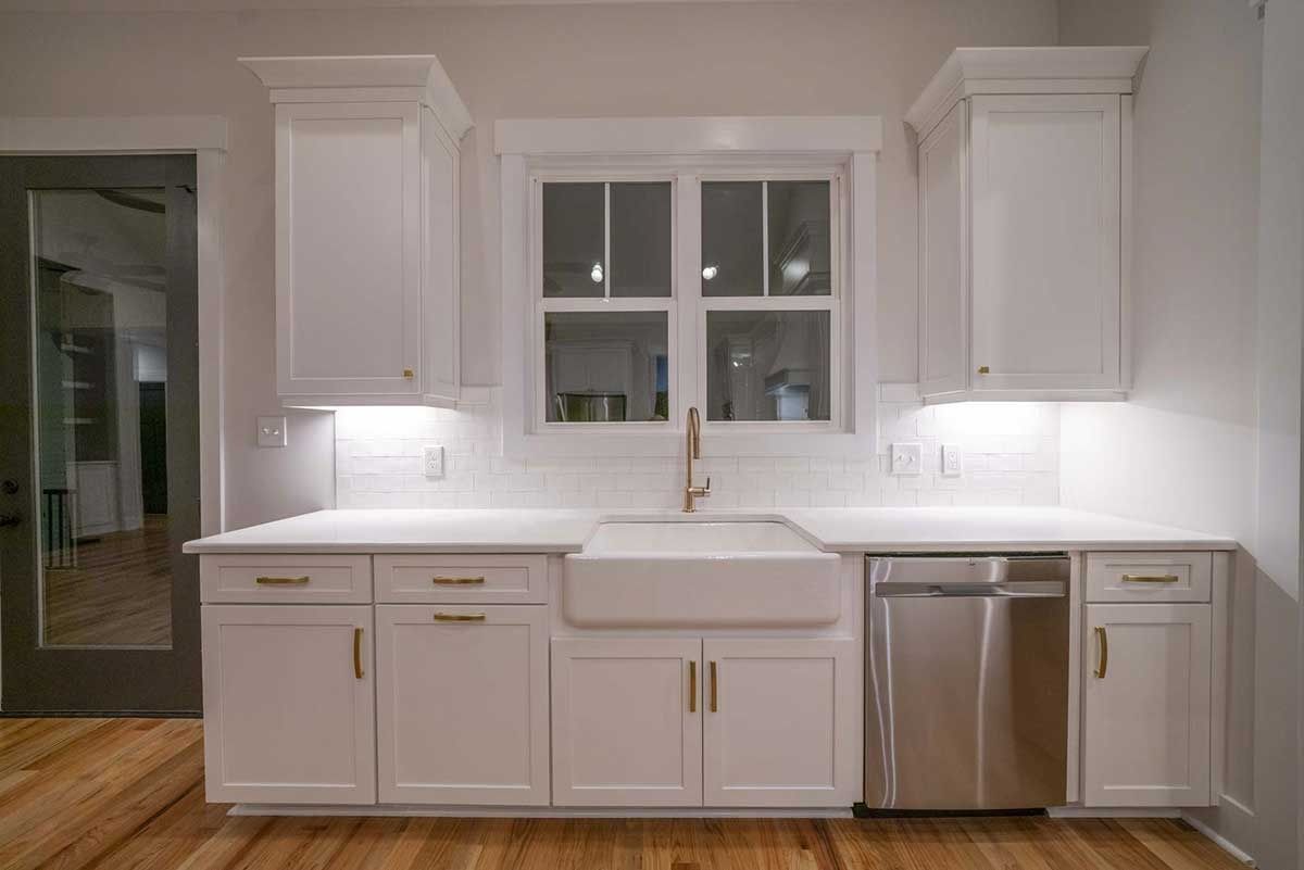 Bright white kitchen with cabinets, window, and stainless-steel dishwasher on wood floor.