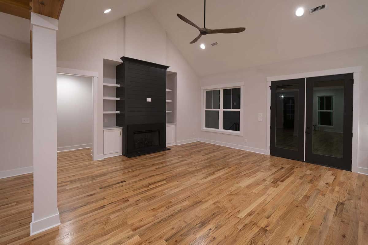Empty modern living room with hardwood floors, white walls, ceiling fan, fireplace, and sliding glass doors