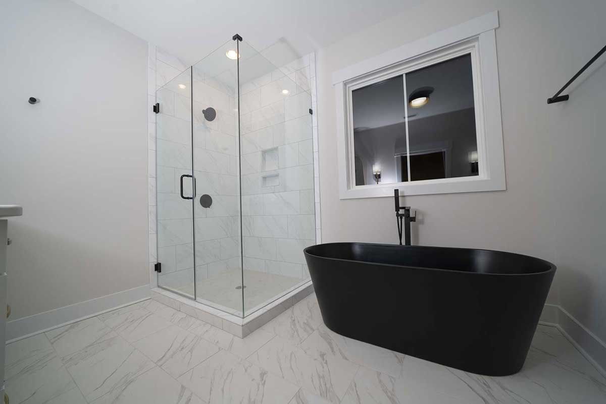 Modern bathroom with glass shower enclosure, black bathtub, and white tile flooring