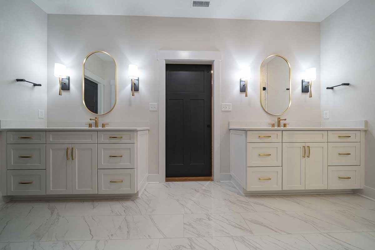 Symmetrical bathroom vanity with two mirrors, wall sconces, and a dark central door on white marble flooring
