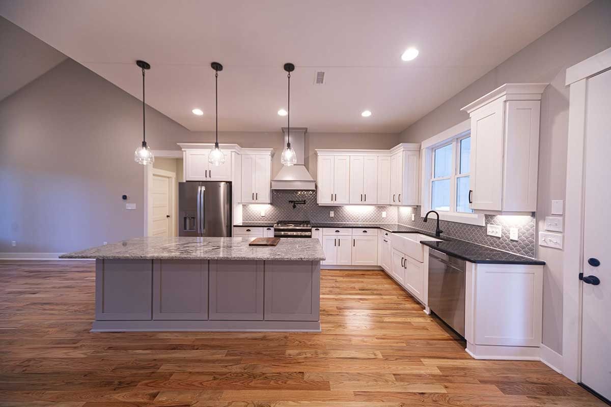 Bright modern kitchen with white cabinets, gray island, hardwood floors, and stainless steel appliances