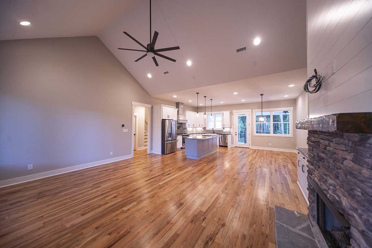 Spacious open-plan living room with hardwood floors, high ceilings, recessed lights, and a stone fireplace.